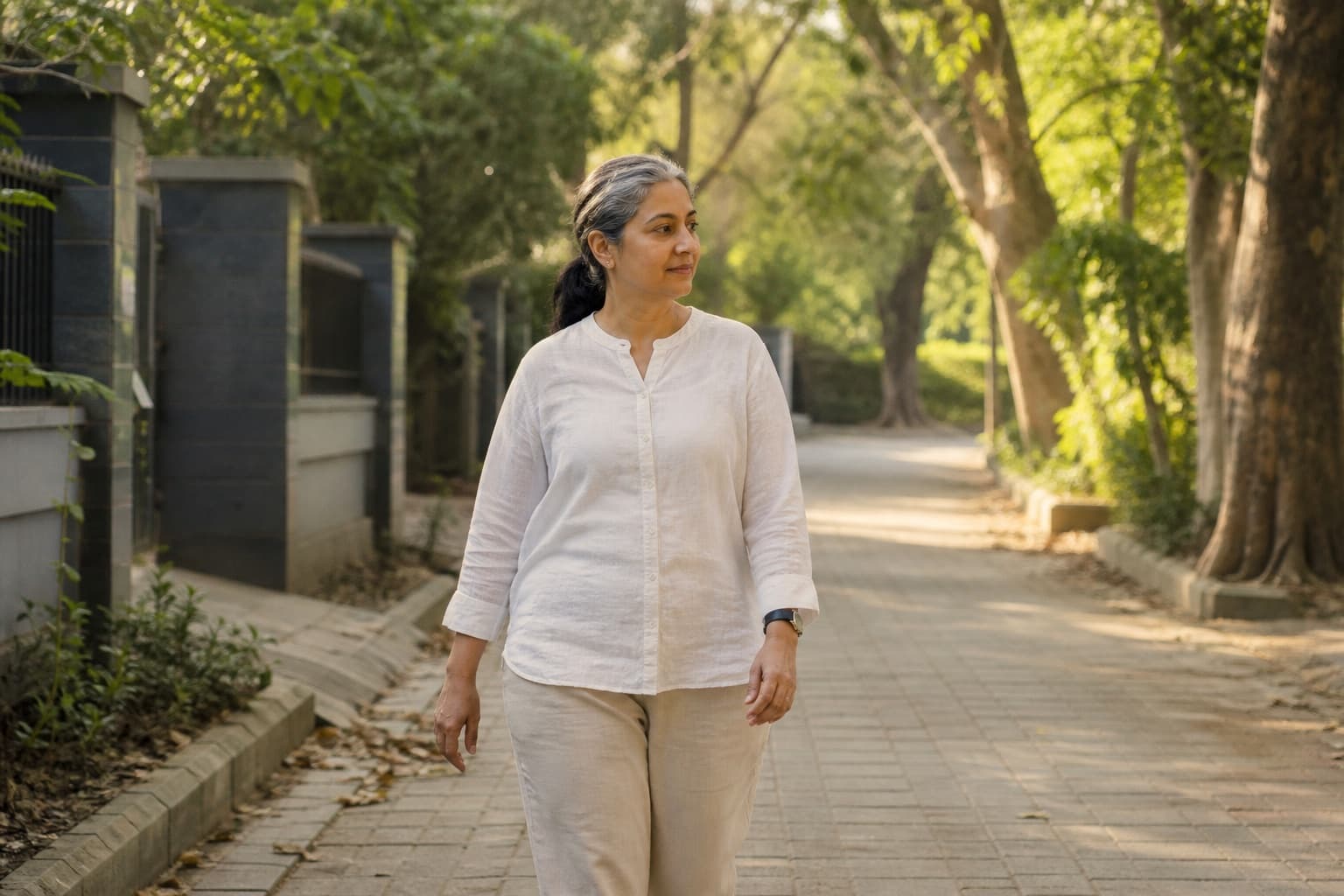 A woman walking unhurried on a tree-lined path in warm evening light